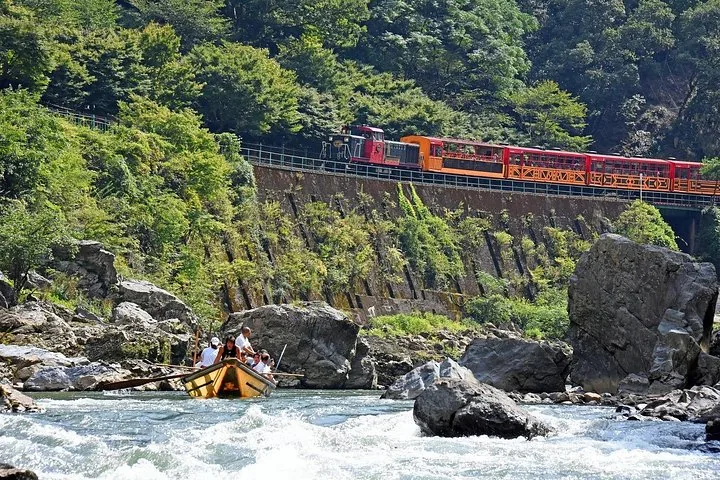 Un train touristique circule sur un pont au-dessus des plaisanciers de la rivière Hozugawa