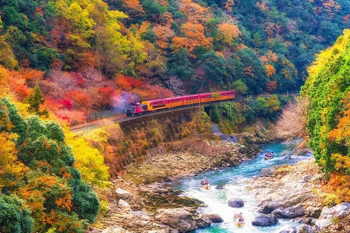 A scenic train and riverboats travel through a valley with autumn colors