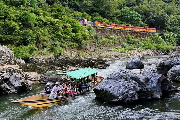 Los pasajeros disfrutan de un paseo en barco por el río Hozugawa mientras un tren pasa por encima